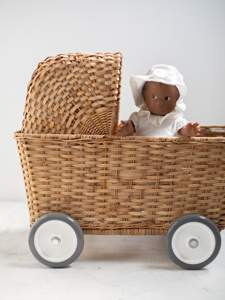 A baby doll with white dress and bonnet sits in a straw carriage.