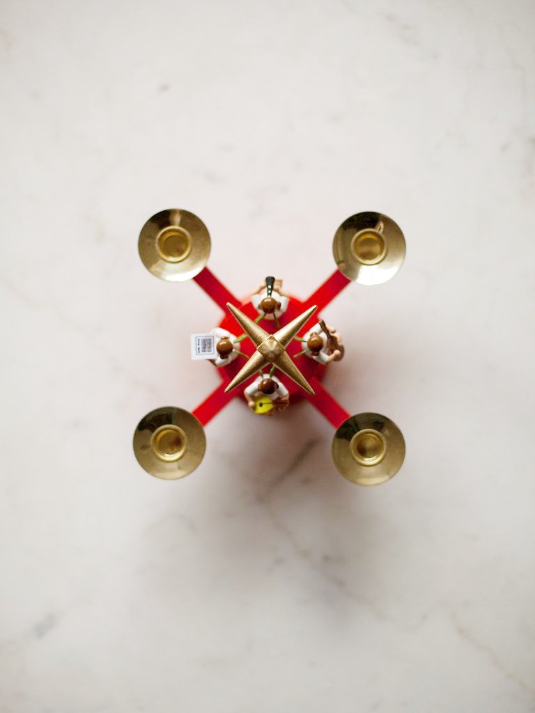 Bird’s eye view of red candleholder. Four gold-colored holders for candles are attached to a red base.