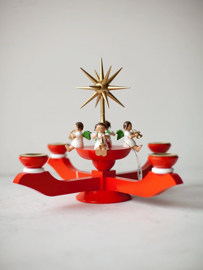 Front view of red Angels Advent Candleholder. The top of candleholder has a gold star surrounded by four angels.