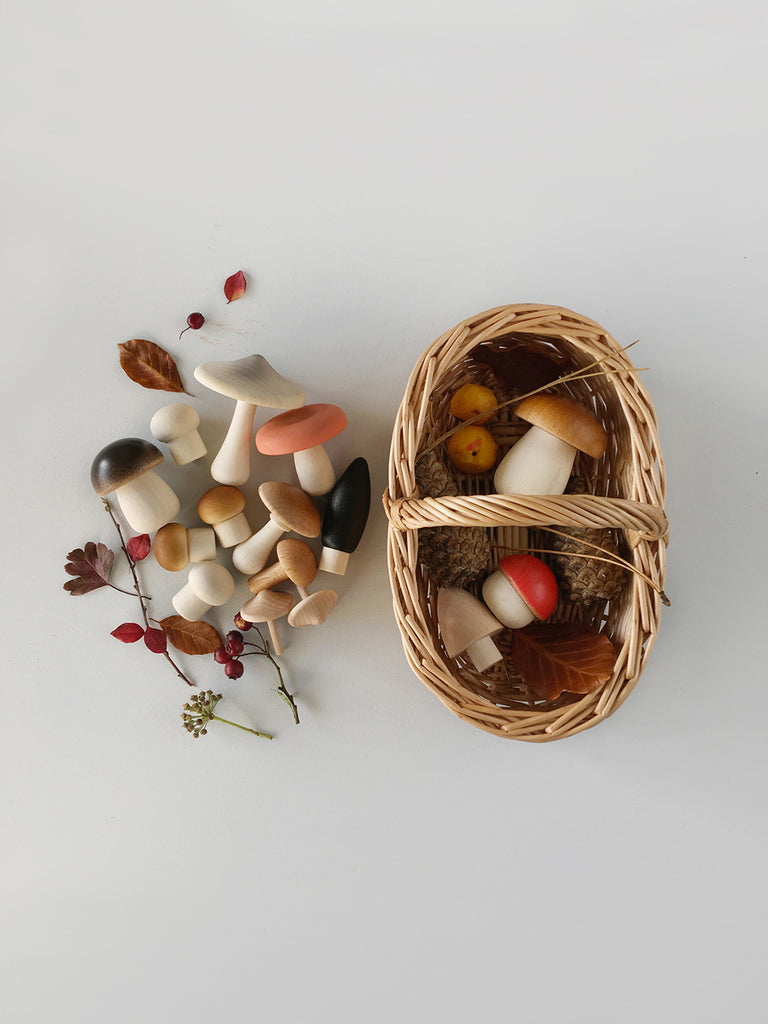  Oval shaped wicker basket with wooden mushrooms, sticks, and pinecones beside and inside it. 
