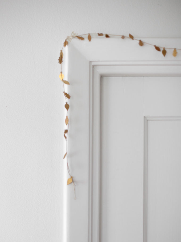 A very thin and bendable piece of brass metal with small thin and flat metal leaf shapes attached throughout the length of it. Hung around the top corner of a doorframe.