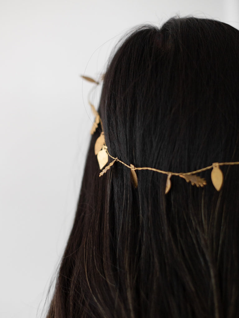 A very thin and bendable piece of brass metal with small thin and flat metal leaf shapes attached throughout the length of it. Placed around the the head of a woman.