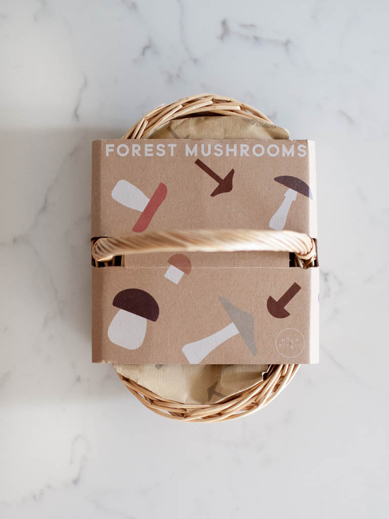 Oval shaped wicker basket in its cardboard packaging seen from the top. Packaging says “Forest Mushrooms” and features little mushrooms scattered on it. 