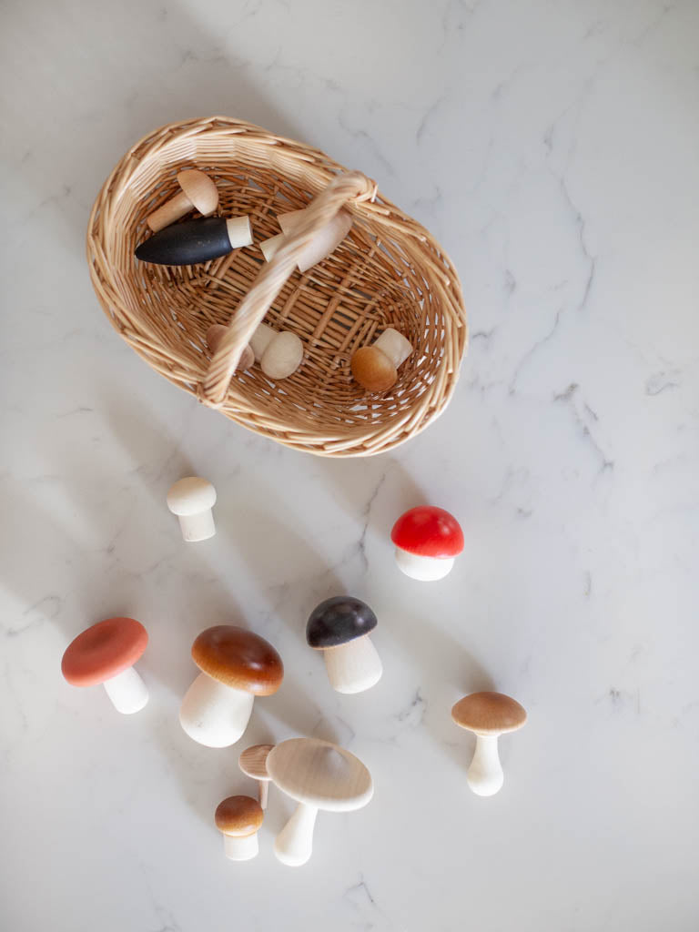 A oval shaped wicker basket with wooden mushrooms inside it and scattered around it. 