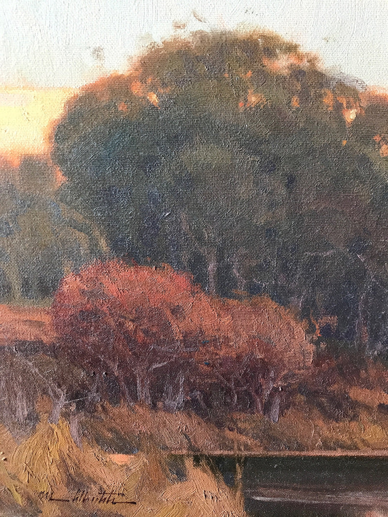 An up close photo of a painting of a tree and a bush in a grassy field behind a sunset. 