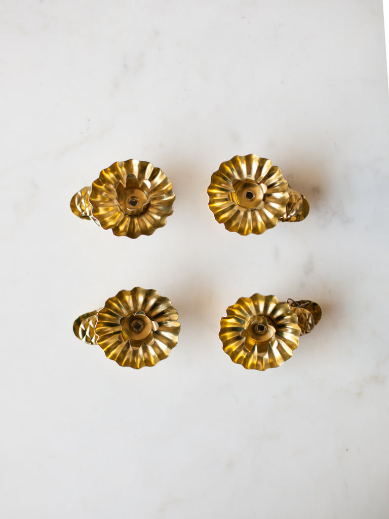 A piece of gold metal in the shape of an open flower, with a space to hold a candle in the middle all sitting on top of a clip.