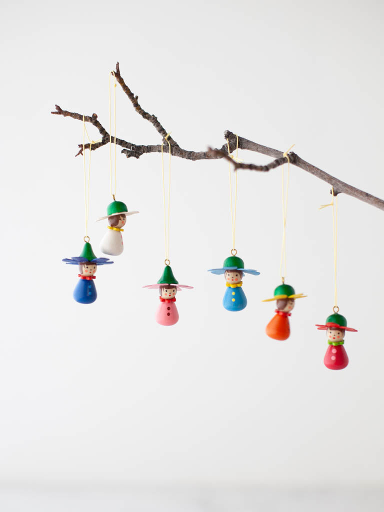 Colorful hanging Flower Children with hats and button ups hung on a branch. 