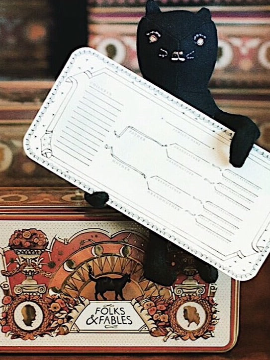 A stuffed cat sitting on the Folks and Fables tin holding up a family tree. 