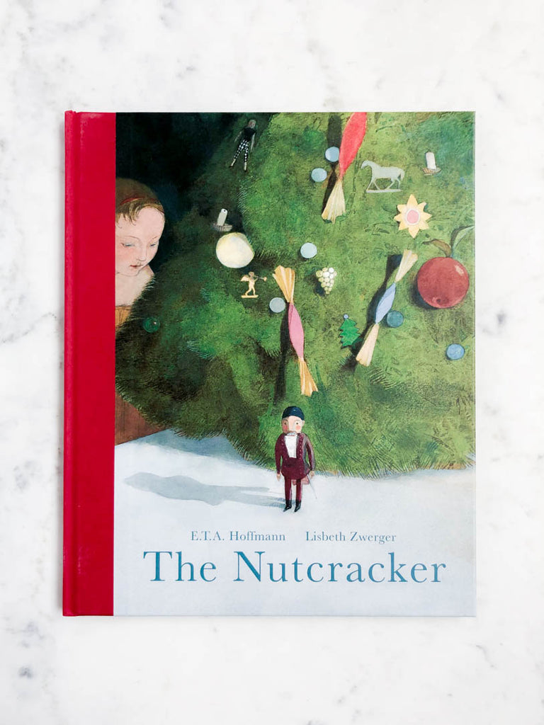 The Nutcracker book lays in full view. A child glimpses around a Christmas Tree with a Nutcracker nearby.