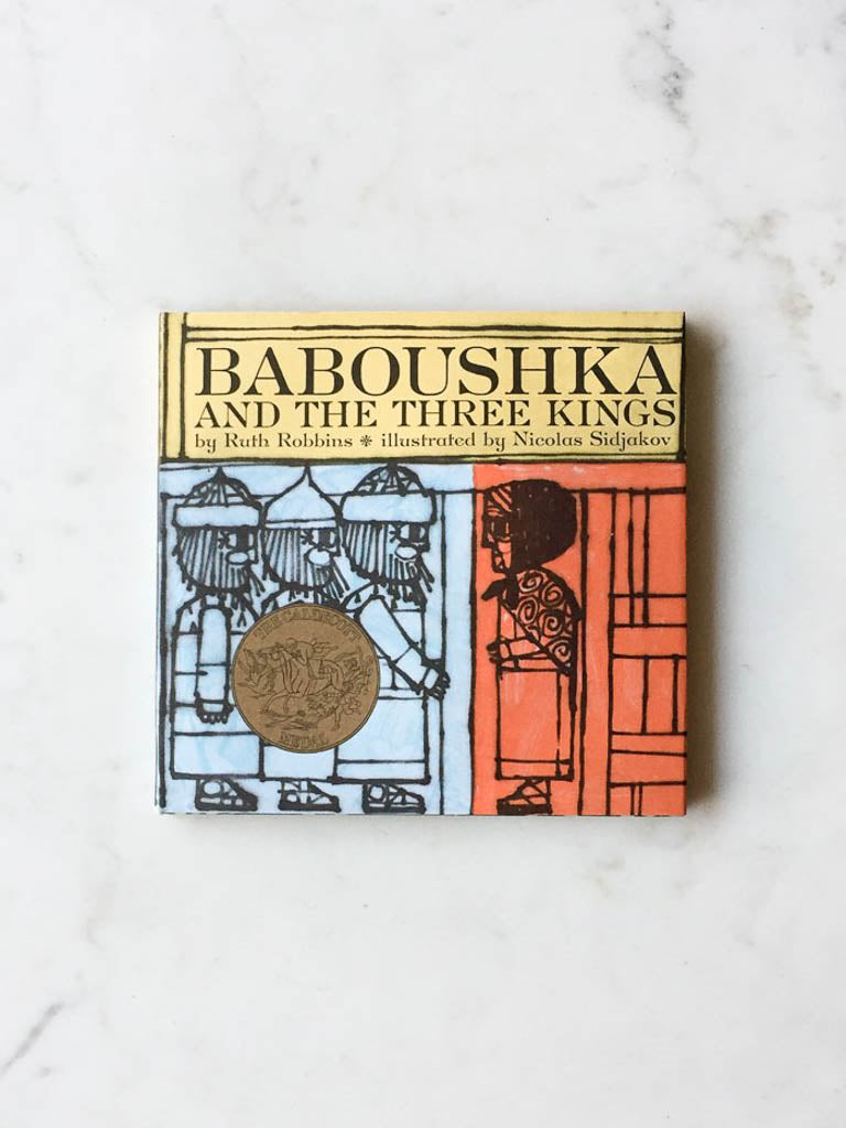 The children’s book has three colors in its cover. Red, yellow, and blue. The cover features block illustrations of the three kings. The book is entitled “Baboushka and the Three Kings”. 