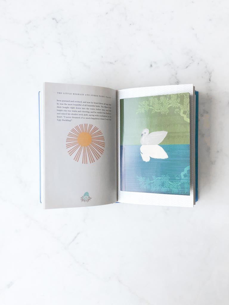 An open page from The Little Mermaid book displaying art of a swan floating on the water and a sun drawing next to the words of the story.
