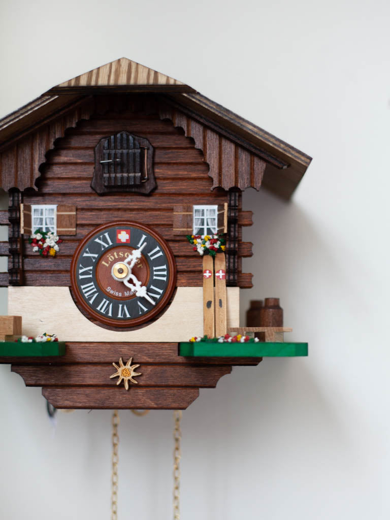 Closeup shot of dark wood ski chalet mechanical cuckoo clock hanging on a wall.
