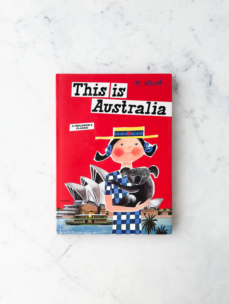 Red childrens book labeled "This is Australia". Image on cover shows woman holding a koala bear in front of Sydney Opera House.