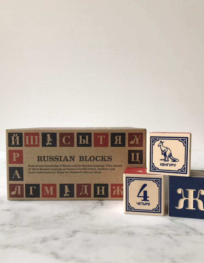 Some blocks decorated with letters, numbers, and animals on their sides with the box they come in behind them titled “Russian Blocks.”
