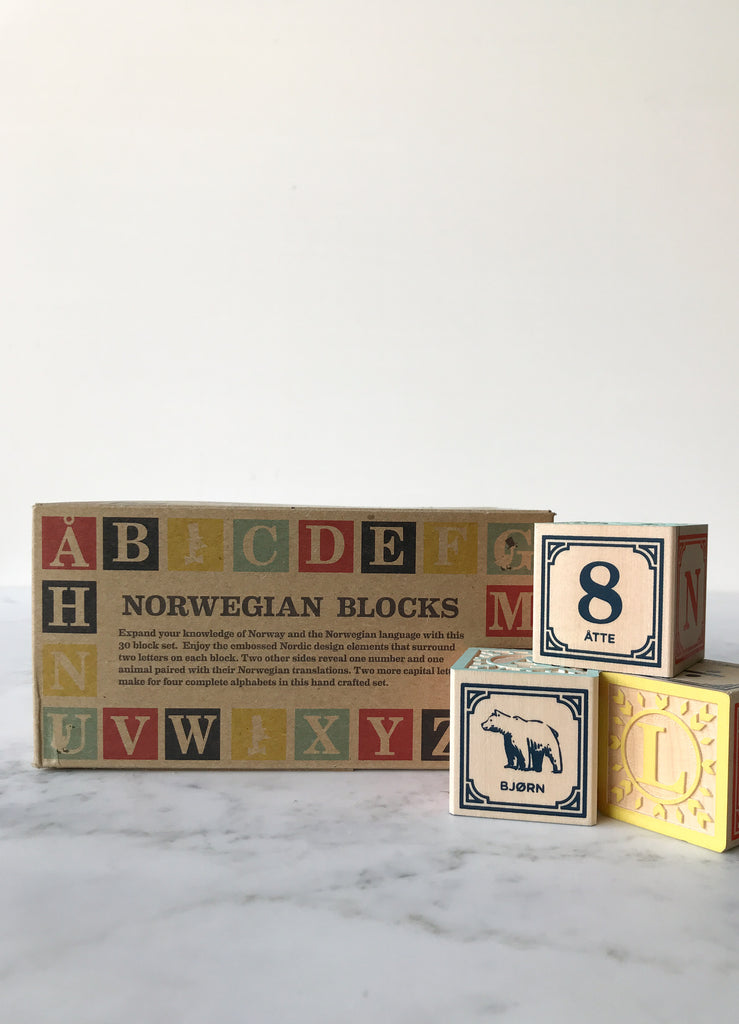 Some blocks decorated with letters, numbers, and animals on their sides with the box they come in behind them titled “Norwegian Blocks.” 