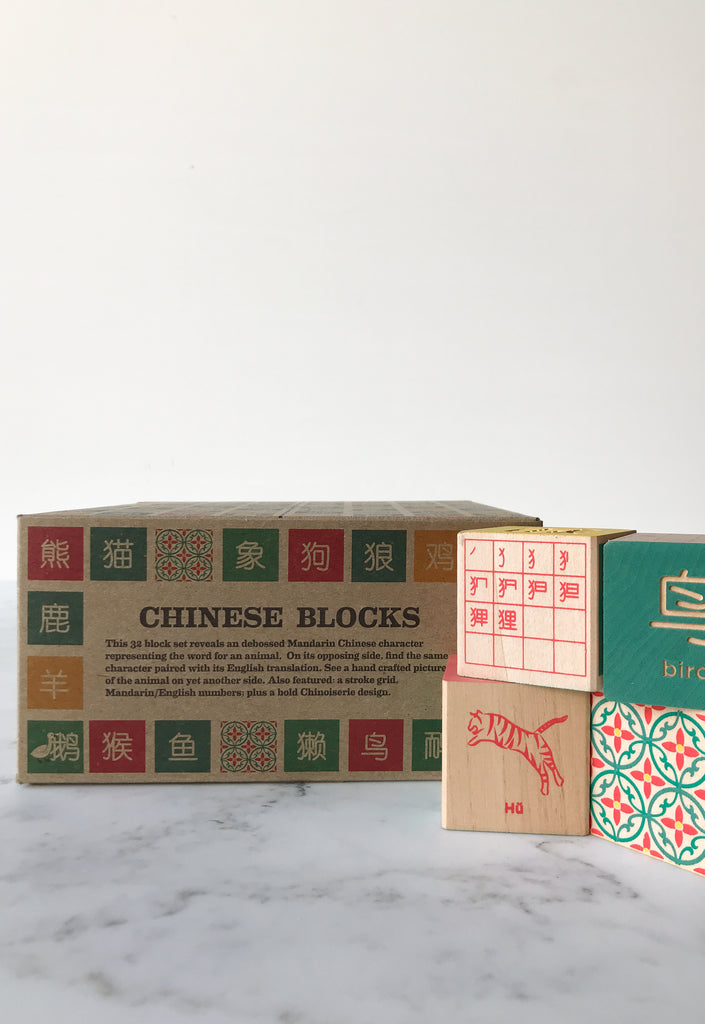 Some blocks decorated with symbols and animals on their sides with the box they come in behind them titled “Chinese Blocks.” 