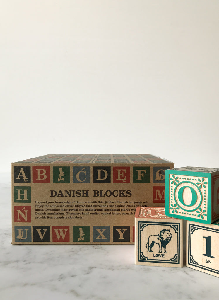 Some blocks decorated with letters, numbers, and animals on their sides with the box they come in behind them titled “Danish Blocks.” 