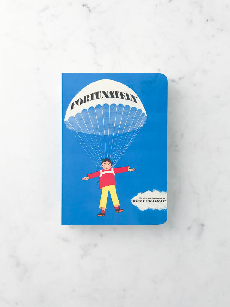 A blue boardbook with an illustration of a boy floating by a parachute with the title “Fortunately.”  