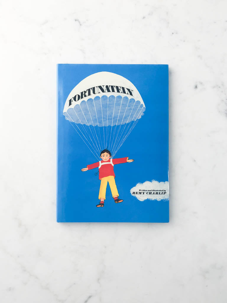 A blue book with an illustration of a boy floating by a parachute with the title “Fortunately.”  