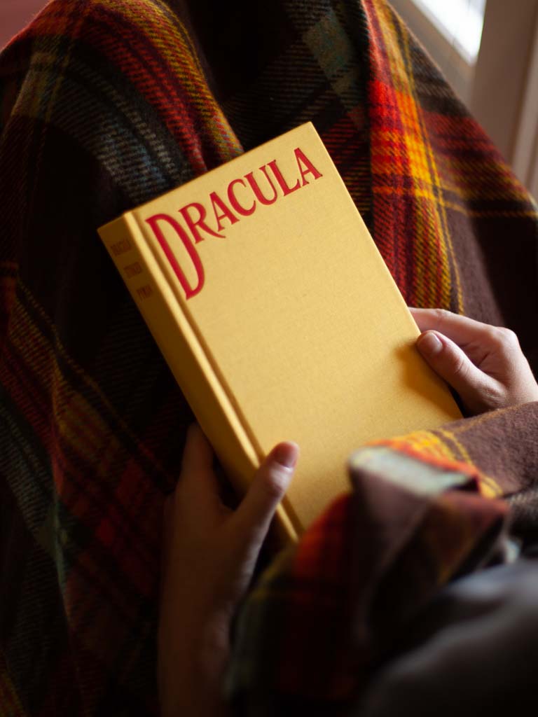 Person wrapped in a blanket holding a copy of Dracula. 