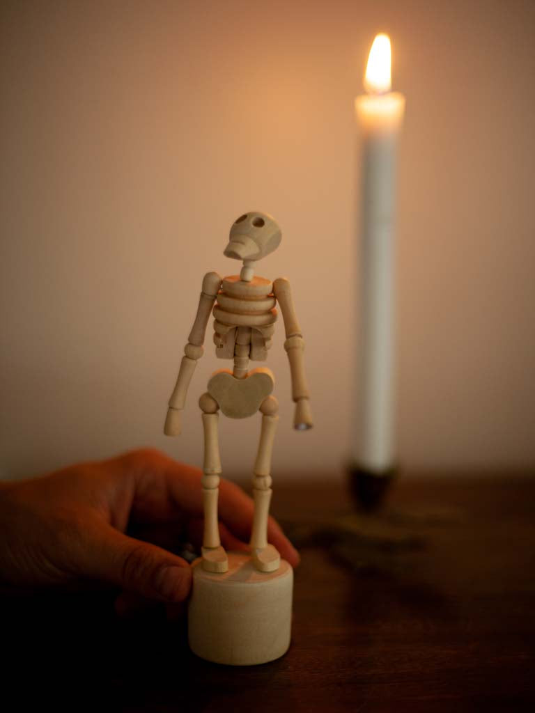 A small wooden moveable figure of a skeleton by a candle. 