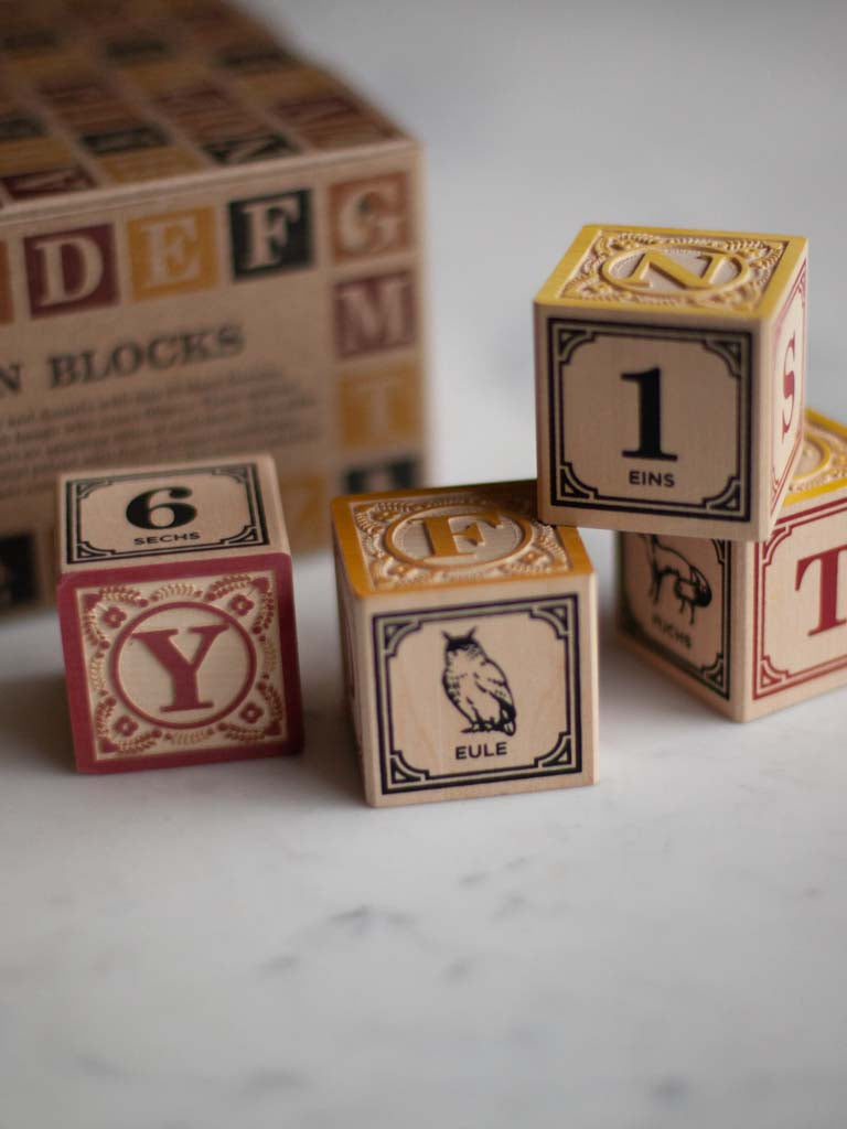 Some blocks decorated with letters, numbers, and animals on their sides with their box they come in behind them. 