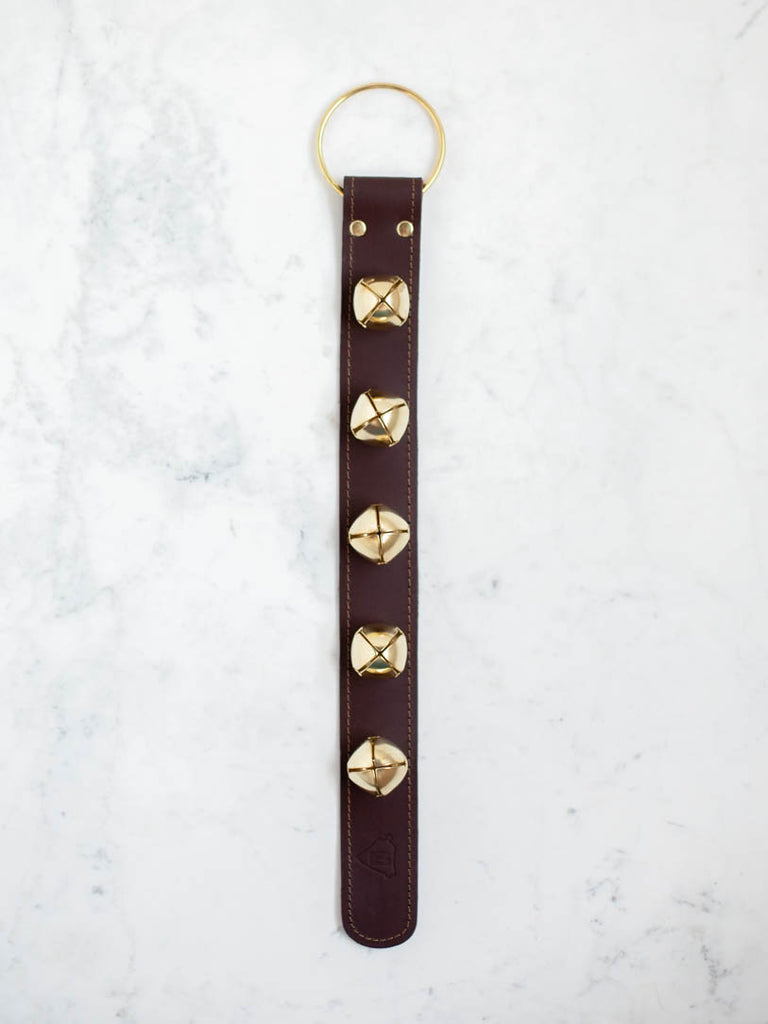A leather strap with sleigh bells on it with a gold hoop at the top. 