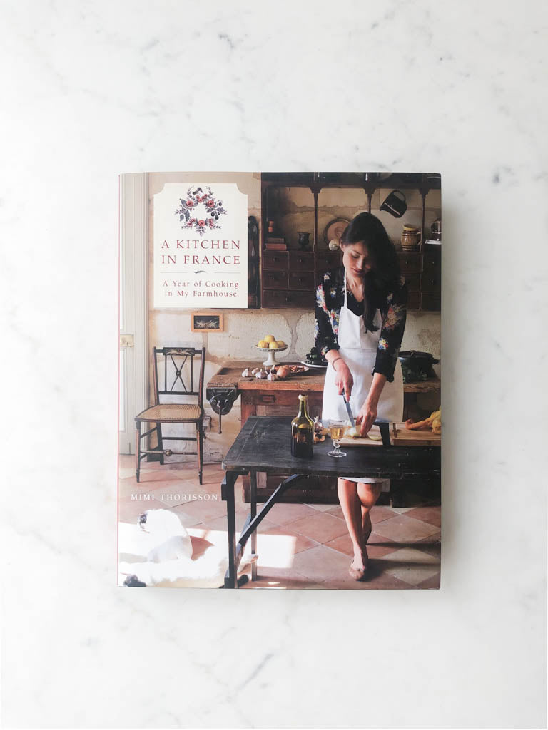 Book cover labeled "A Kitchen in France" with image of french woman cooking in her kitchen