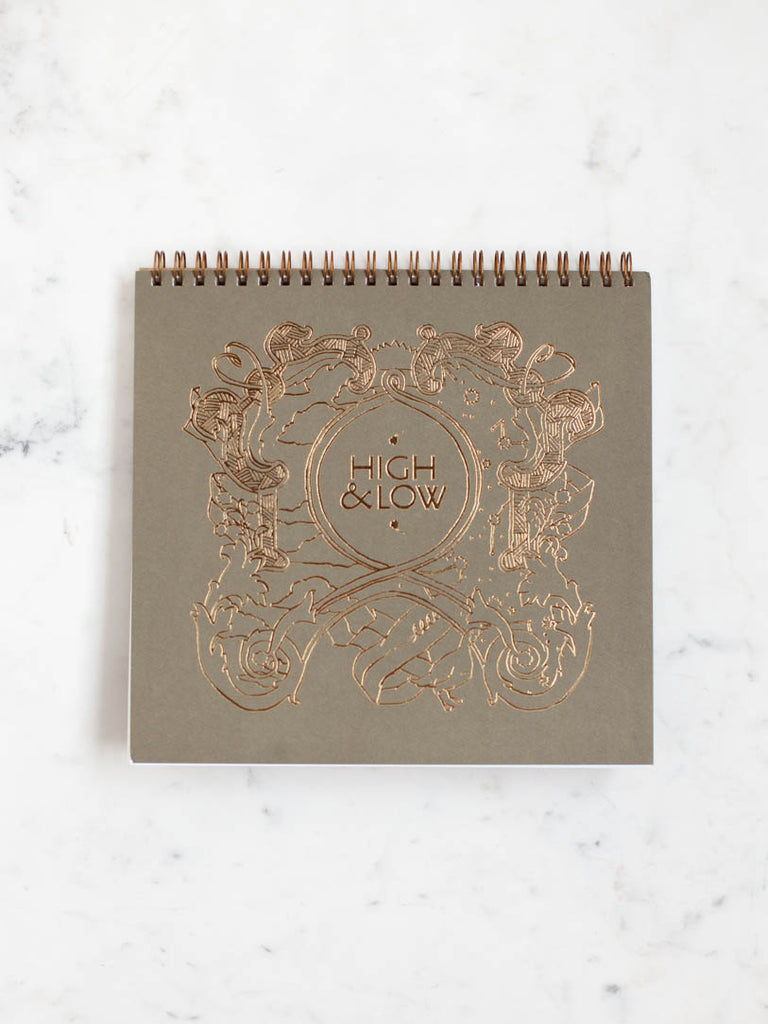 The top cover of the inside notebook, the same design at as the box cover but with a dark green background and drawn in gold color.