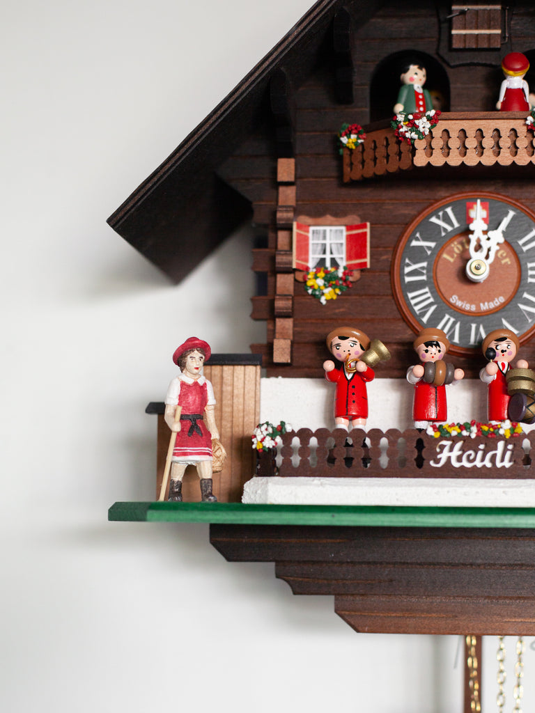 A dark wood Swedish cuckoo clock containing four wooden figurines playing instruments on the front. Includes small red details and other small figurines including a dog and the circulating group of figurines at the top of the clock.