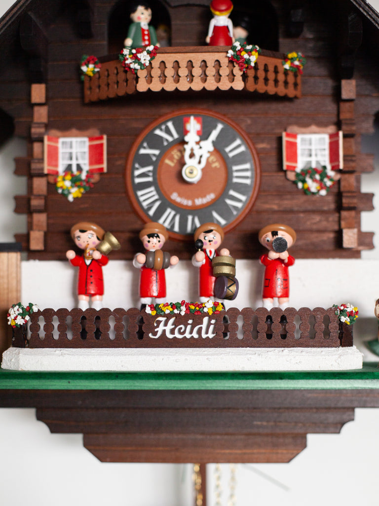 A dark wood Swedish cuckoo clock containing four wooden figurines playing instruments on the front. Includes small red details and other small figurines including a dog and the circulating group of figurines at the top of the clock.
