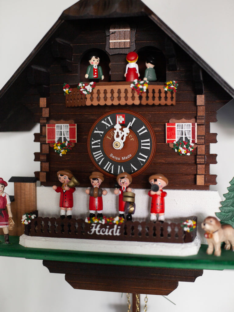 A dark wood Swedish cuckoo clock containing four wooden figurines playing instruments on the front. Includes small red details and other small figurines including a dog and the circulating group of figurines at the top of the clock.