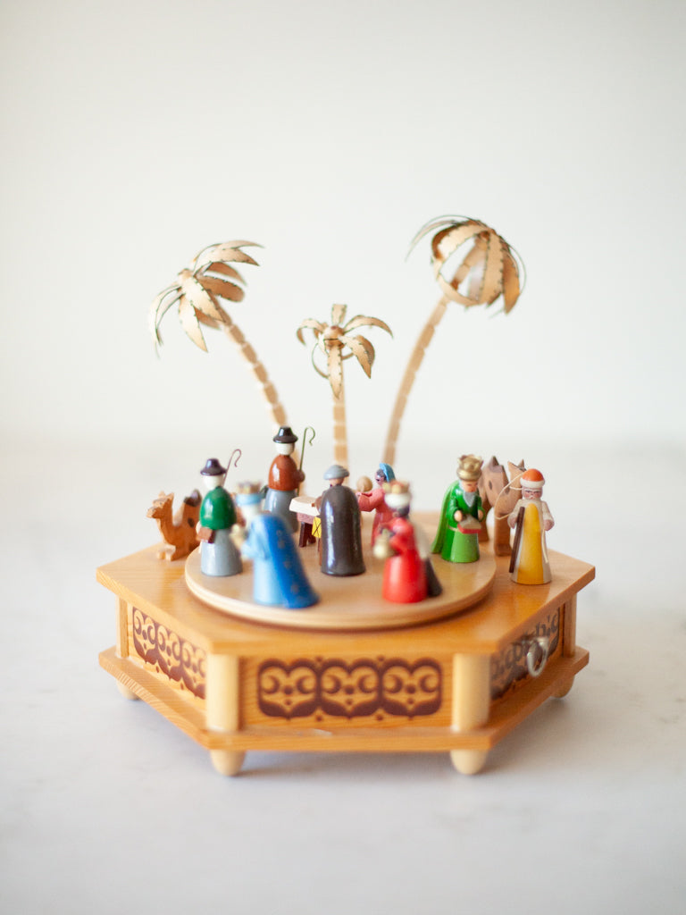 Side view of the antique nativity music box. The figures are clad in the colors of red, green, and blue. The figures are position on top of a moving pine base.