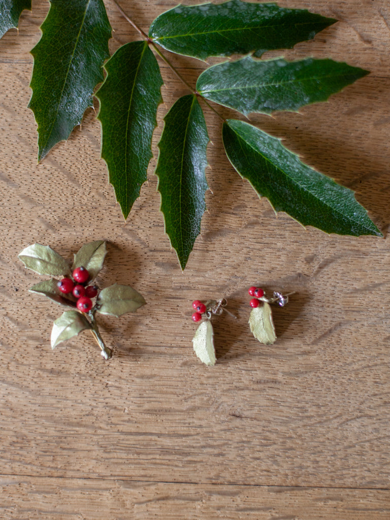 The brooch and the earrings of the holly jewelry, both including red berries and green leaves.